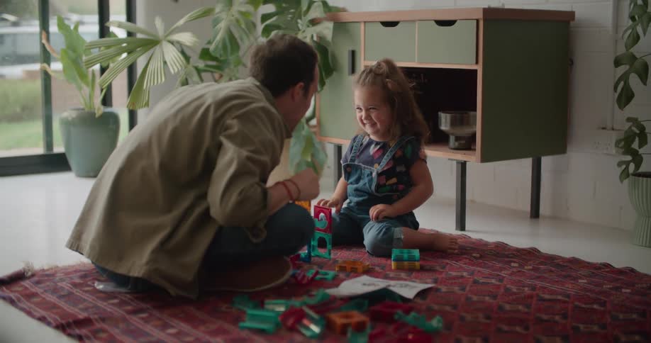 A dad and his daughter high five after building with blocks on the floor