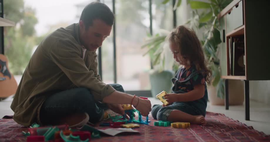 A man is sitting on the floor with a little girl playing with toys