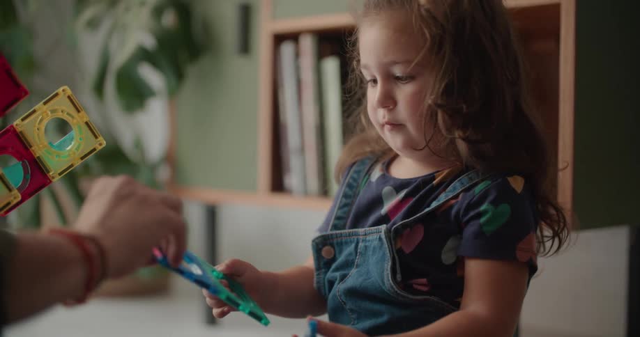 A young girl plays with a toy set while sitting on the floor with an adult