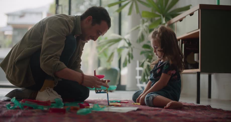 Father and daughter on a blanket on the floor playing with colorful plastic toys