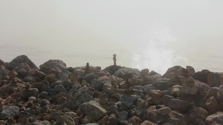 Sun glints off water near rocky shore dotted with stacks of stones