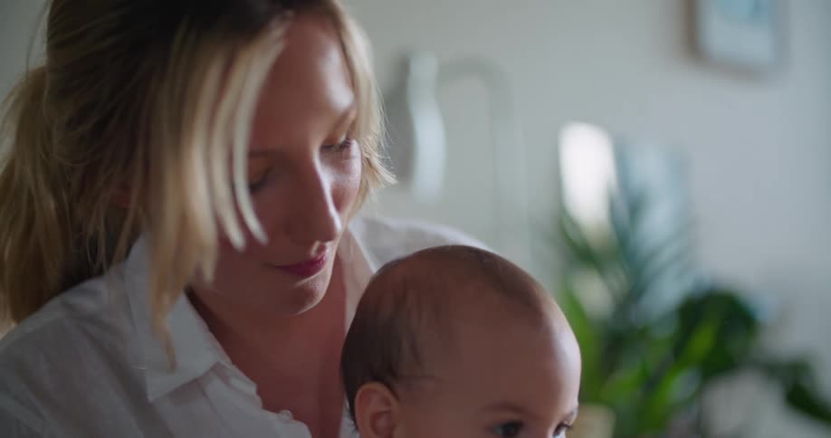 Mother holds baby on her lap smiling and watching then jiggling him as he reaches