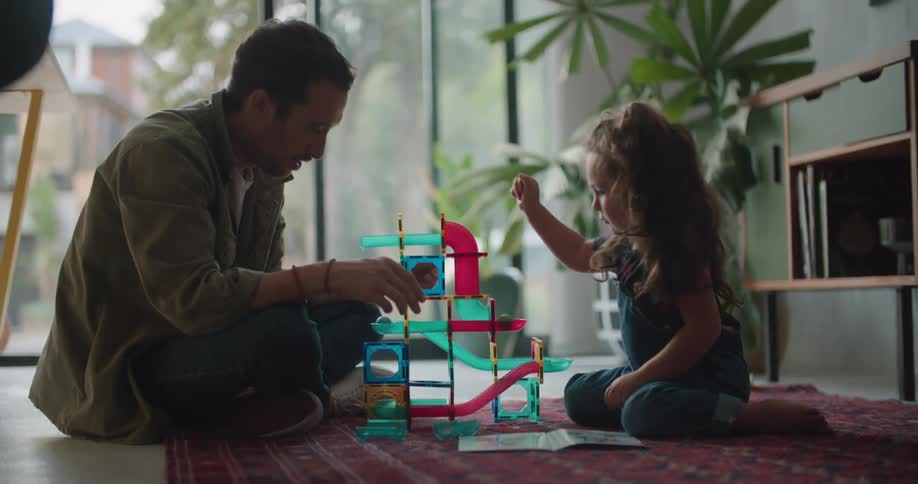 A man is sitting on the floor with a little girl playing with toys