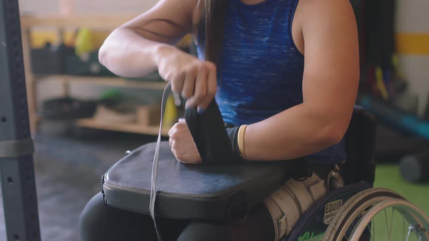 A woman in a wheelchair wraps her wrist as she prepares to workout in the gym