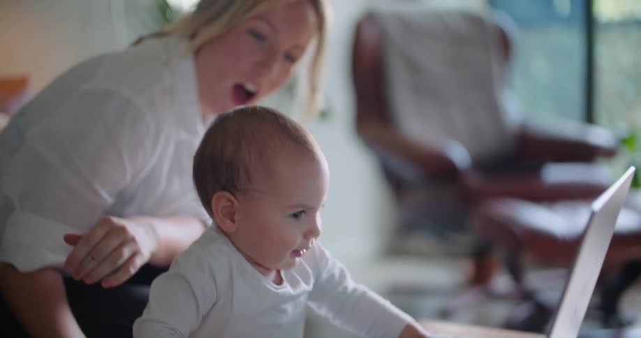 A woman laughs in surprise after showing her baby how to stand and use a laptop