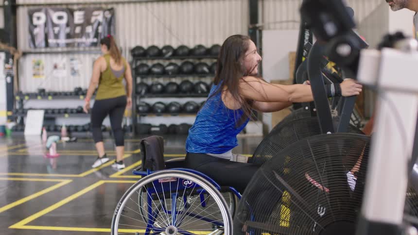 A woman in a wheelchair works with a personal trainer in a gym
