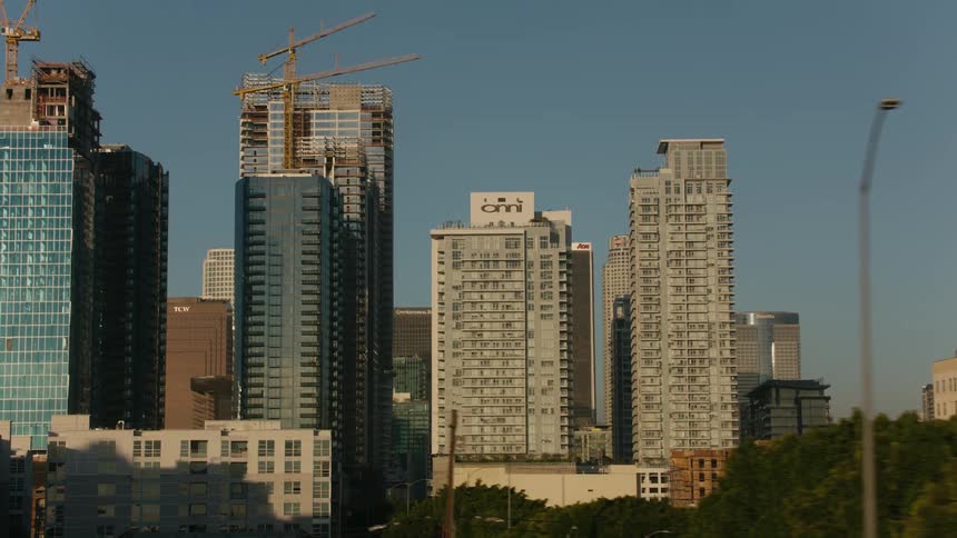 Two construction cranes sit on top of skyscrapers under construction in the city on a sunny day
