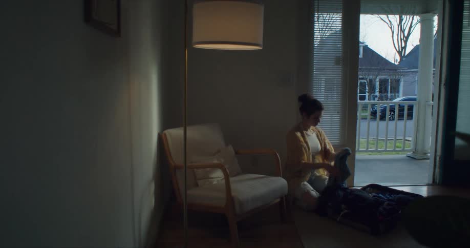 A woman kneeling near an open door folding and packing clothes