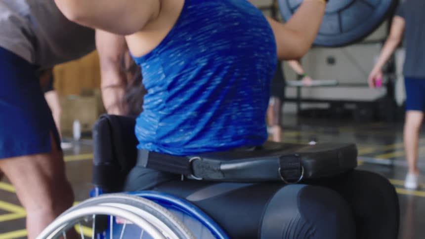 Female weightlifter on a wheelchair lifting a heavy barbell over her head multiple times at a gymnasium