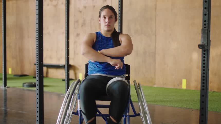 Woman sitting in wheel chair roll her chair forward between metal struts and crosses her arms