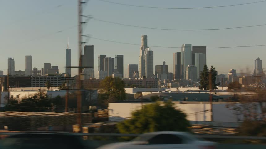 Traveling past buildings where tall city towers can be seen in the distance under a clear sky