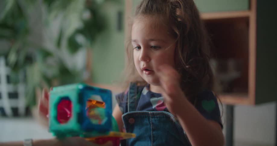 An adult holds a toy while a young girl attaches a missing piece