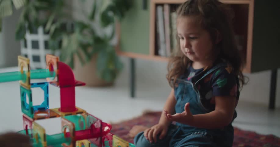 A young girl watches as a ball rolls down a toy set