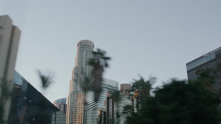 Traveling past trees where tall city towers can be seen under a clear sky