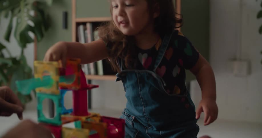 Daughter with curly hair and mother sitting on the floor play with toys in living room at home