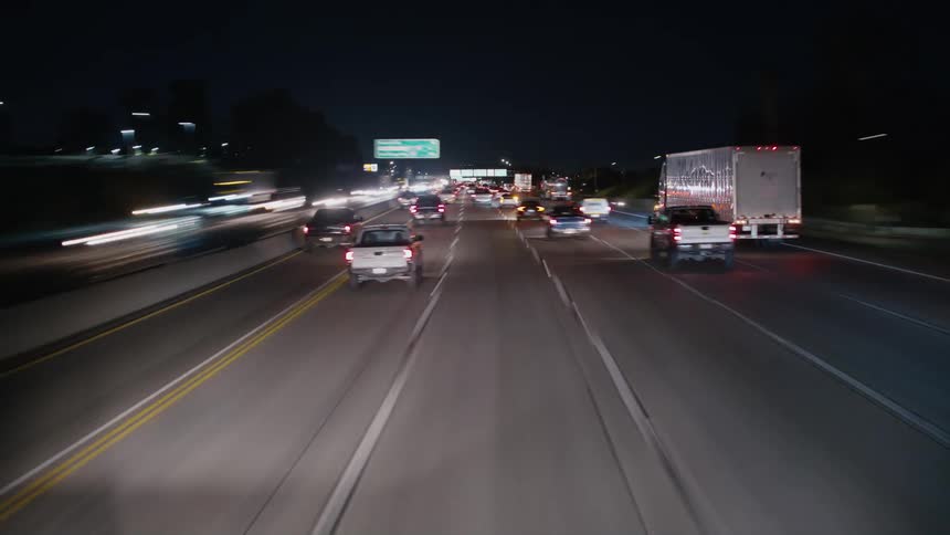 Tail lights and headlights shine as traffic moves on a busy highway at night