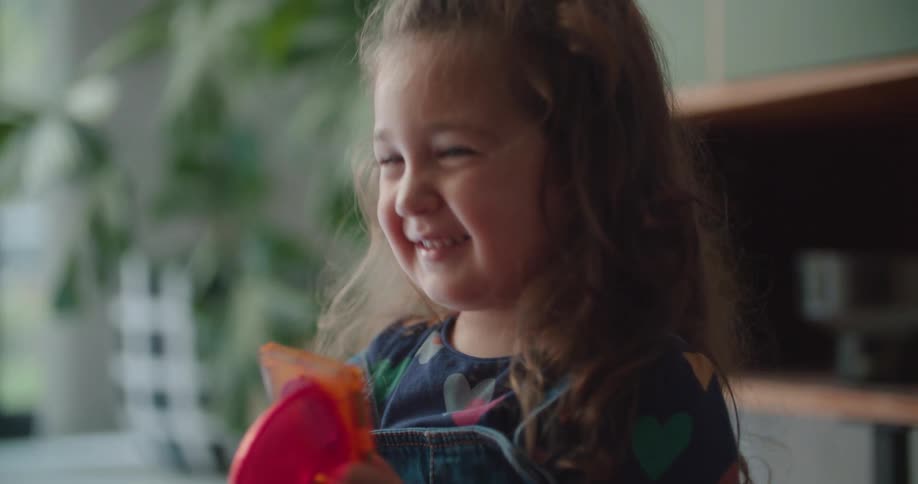 A little girl is holding a toy as she talks and smiles