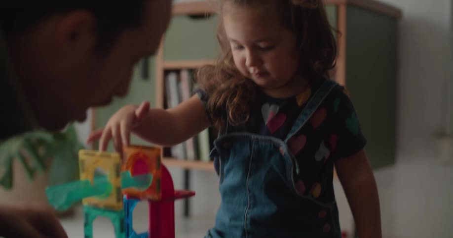 A man is sitting on the floor with a little girl playing with toys