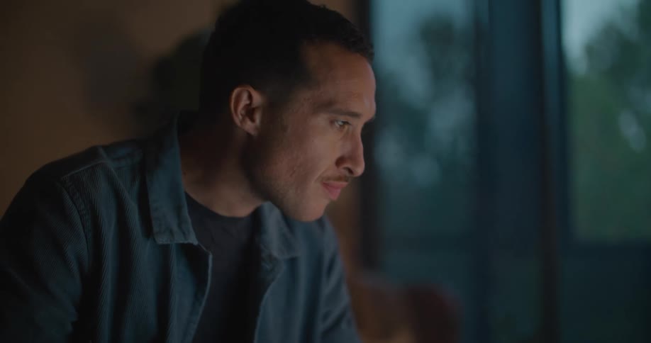 A man is eating food indoors while the sun is setting