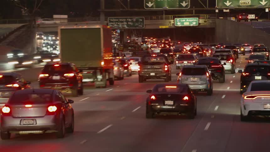 Dense traffic moves along a freeway on the outskirts of a city in the evening