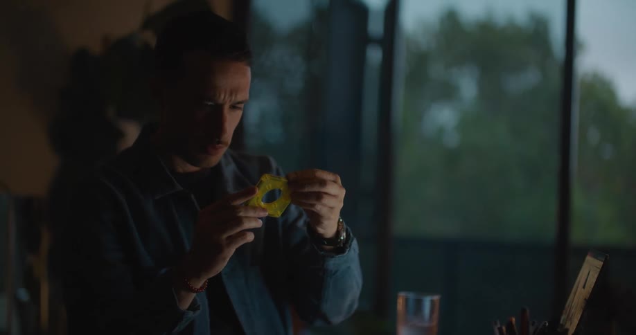 Man holding a square cassette looks at it then looks at a laptop then writes in a notebook