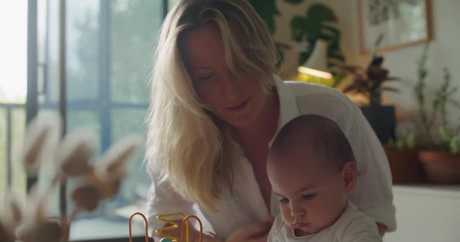 A baby uses a paper and pen on a table being played with by mom