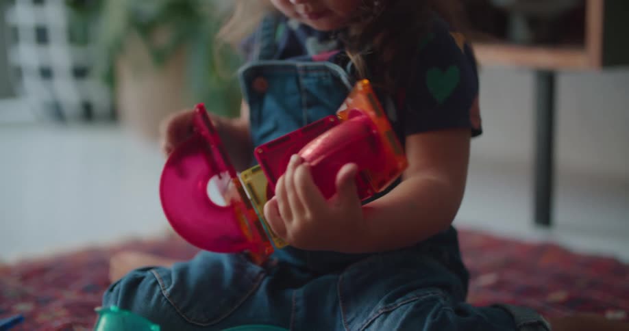 A young girl examines a toy before looking up and smiling at the adult sitting across from her