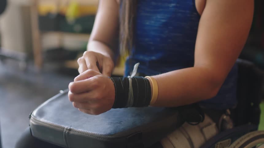 A woman sitting in a wheelchair wraps tapes on her wrists