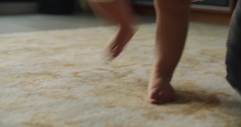 Mother helps baby bounce on his feet on carpet
