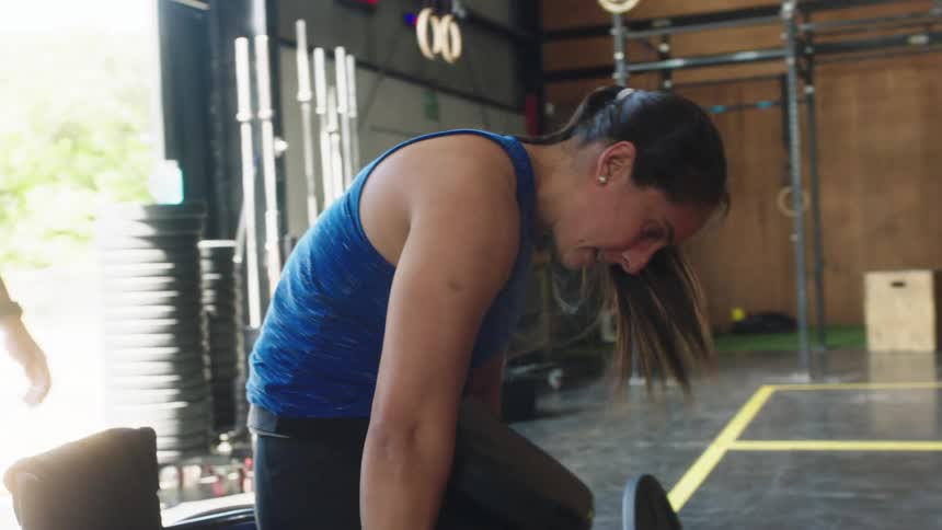 Woman pushes herself up from the floor and into a wheelchair in the gym as a man wearing shorts is nearby