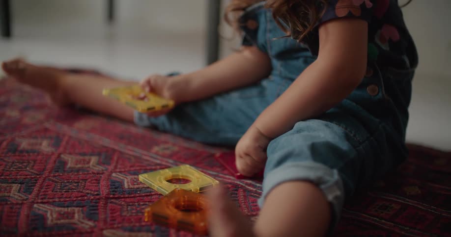 Little girl sitting on the carpet at the floor playing with some toys
