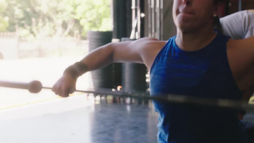A woman exercising lifts a heavy bar over her head