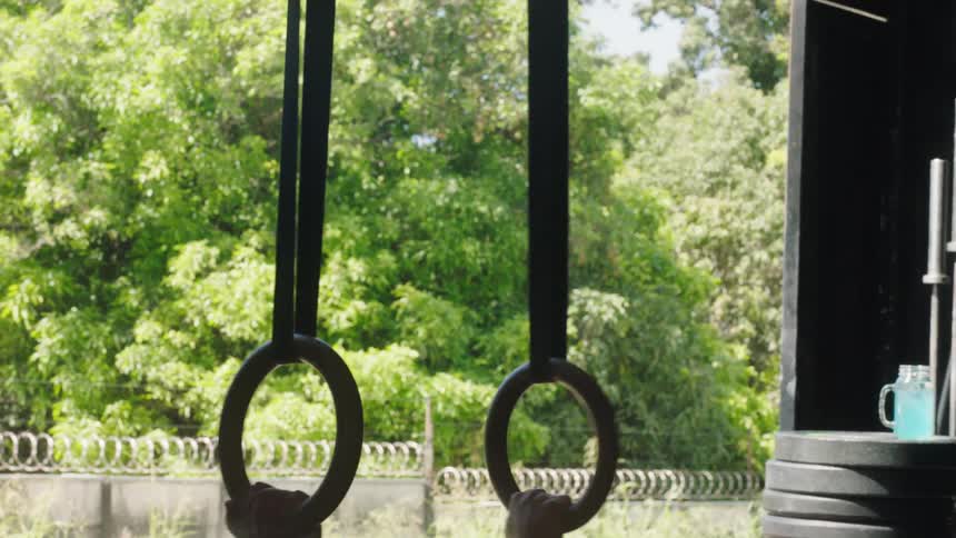 A woman practices upper body exercises on a pair of steady rings in a garage