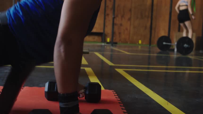 Woman lays on her stomach with a weight in each hand and pushes herself up from the gym floor
