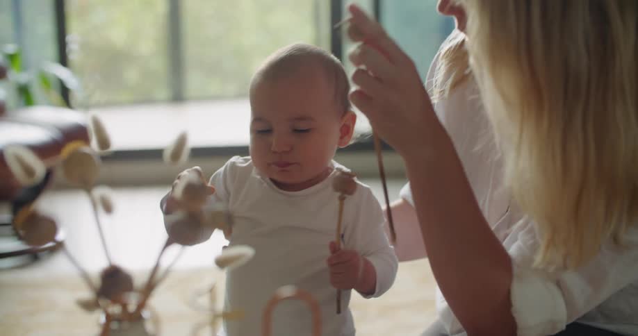 A baby is taking flowers out of a vase and putting them in their mouth as a woman takes the flowers