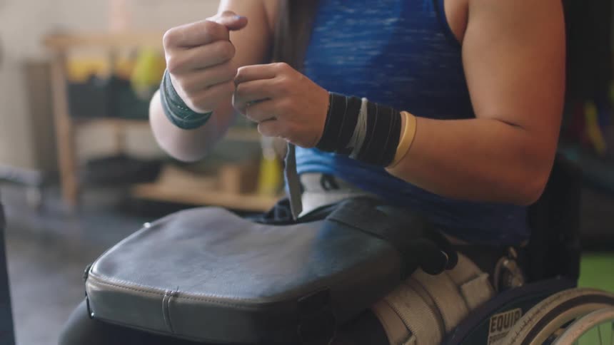 Woman sitting in wheel chair in the gym wraps her wrists