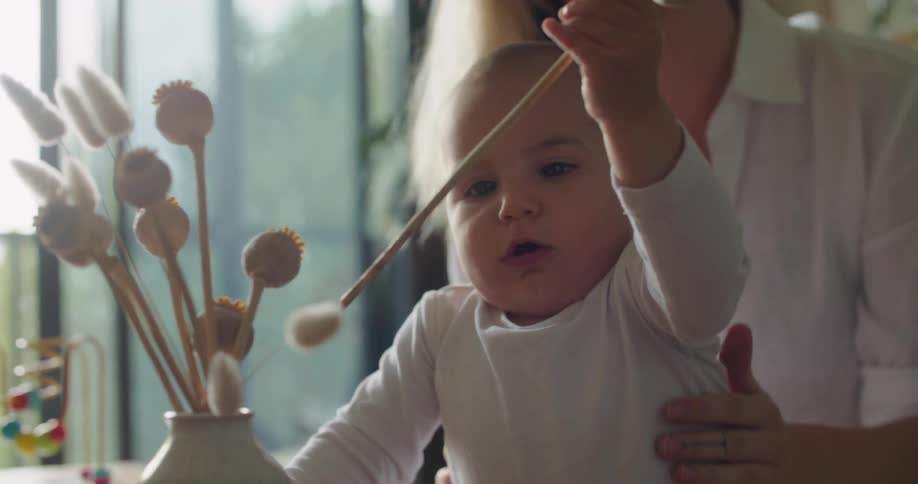 A woman prevents a baby from falling as he retrieves a flower from a vase