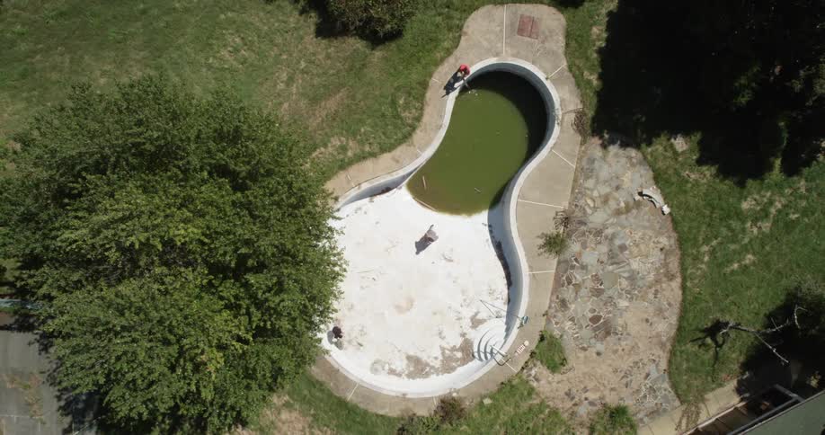 Two people skateboard in an empty pool