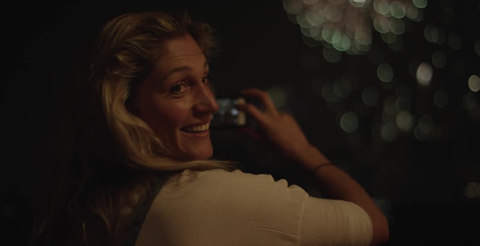 A woman smiles and talks to someone as she films fireworks with her cellphone
