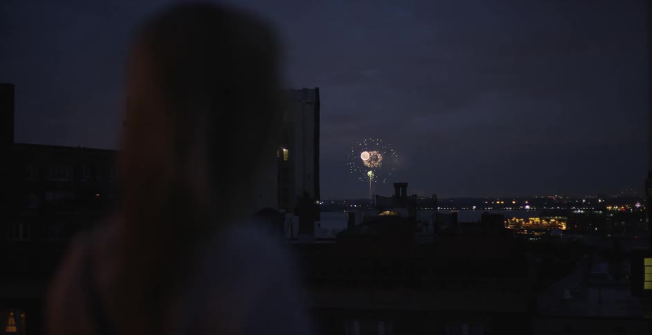 A woman looking out over the city as fireworks explode in the sky