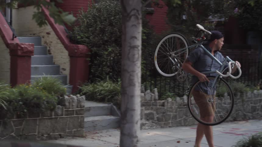 A man emerges from a basement apartment with a bicycle in hand
