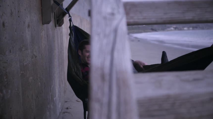 A man reclining in a hammock and waving a polaroid picture while a woman lies next to him