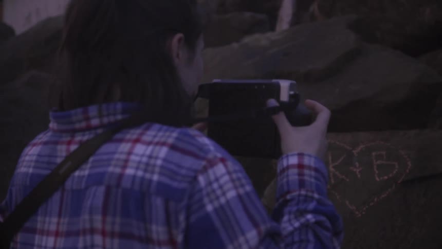 A woman takes a picture of initials on a rock