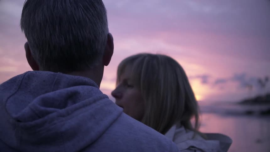 A man and woman stand together on the beach at sunset