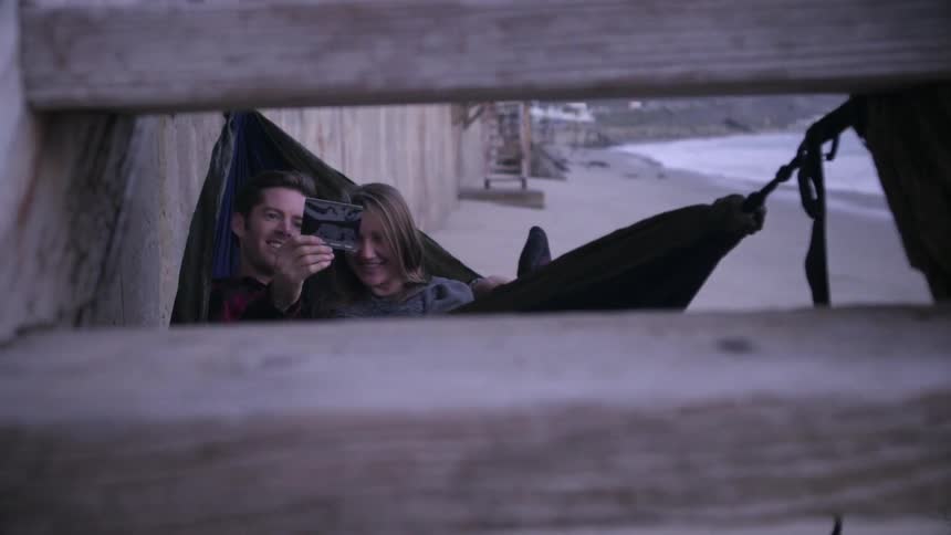 Man and woman sway in a hammock while looking at a photo