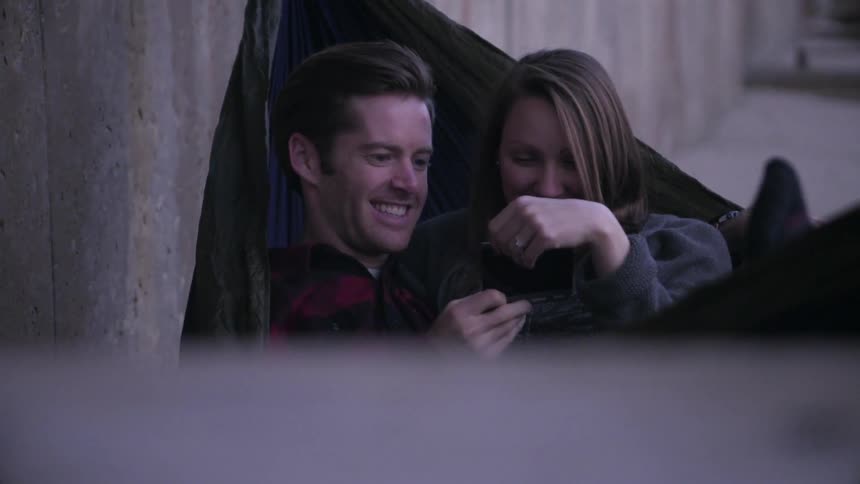 A man and woman smile as they lay in a hammock together