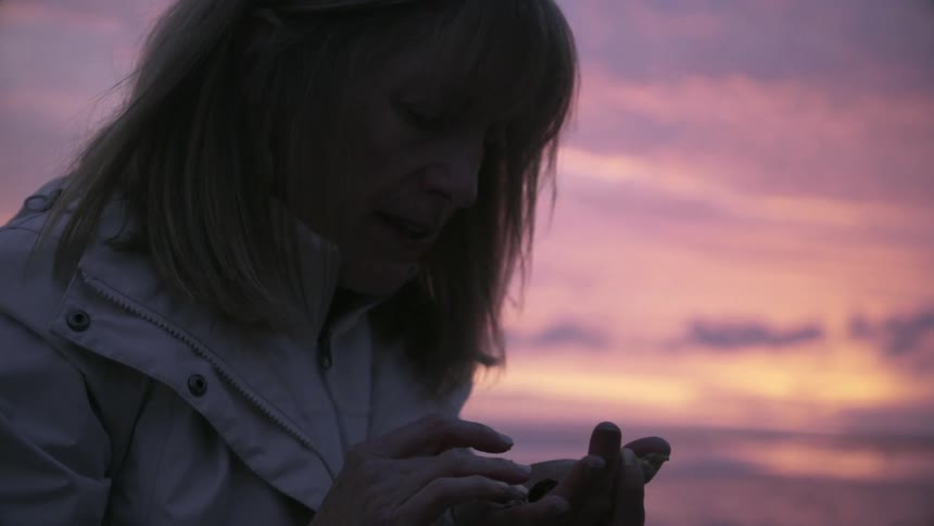 A woman is looking at items in her hand at sunset