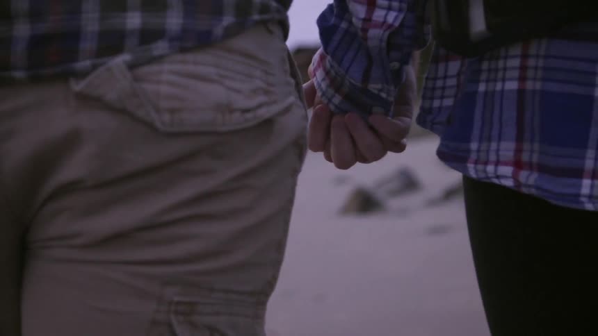 A couple walks down the beach holding hands