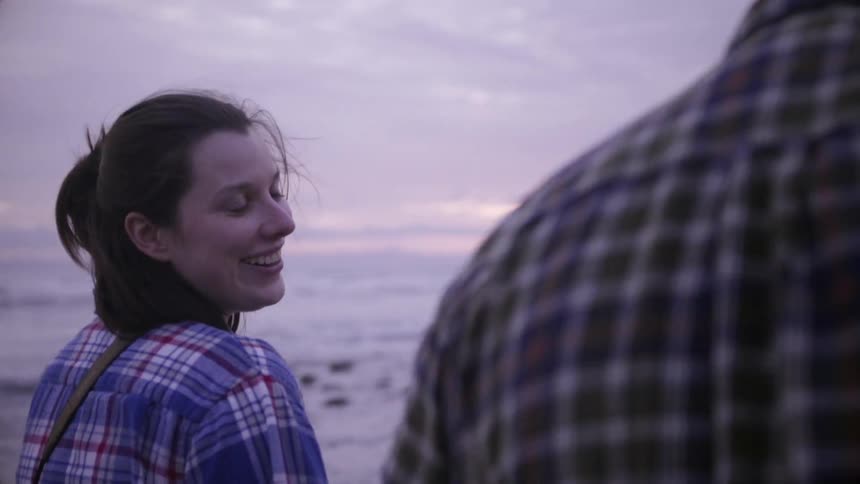 A woman looks over to a man smiling as they walk on the beach