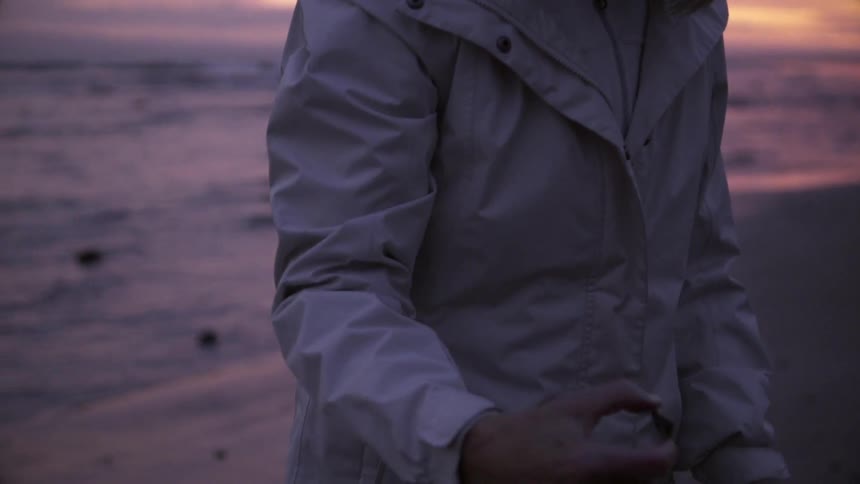 Woman holds and examines a pebble on a beach at sunset